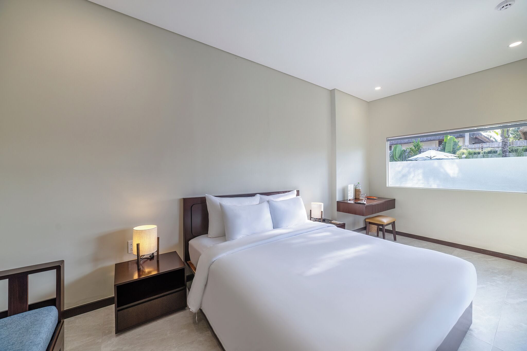 Une chambre d’hôtel avec un grand lit, des tables de chevet, une petite table, une chaise et une fenêtre donnant sur un paysage verdoyant.