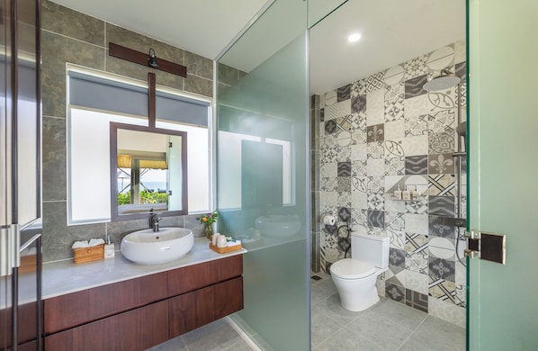 A modern bathroom with a glass shower enclosure, a large mirror, and a vanity with a sink and toiletries. - Coco Cottage Beachfront Resort (Mui Ne)