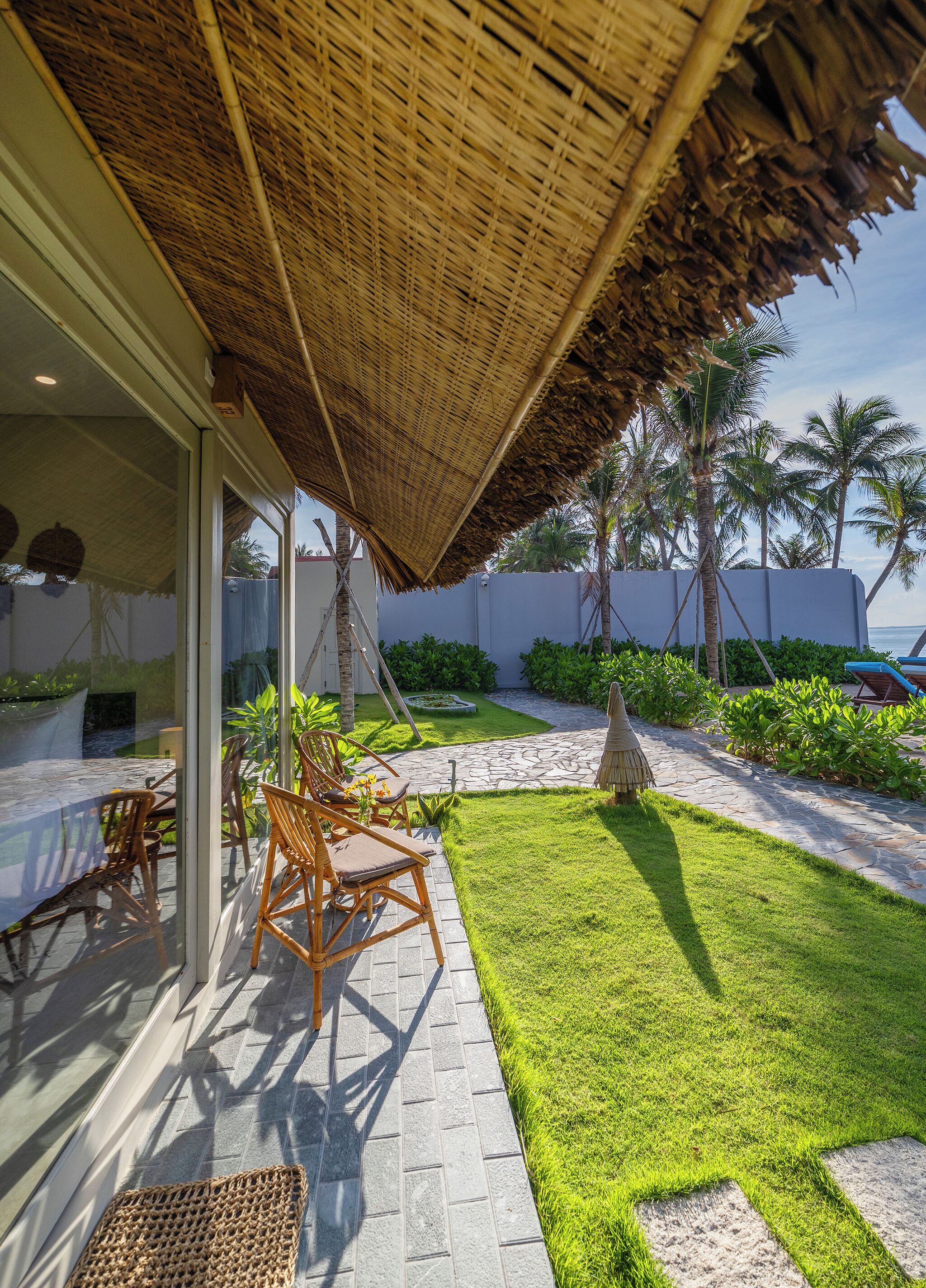 An outdoor patio with a thatched roof, wicker furniture, and a well-maintained lawn.