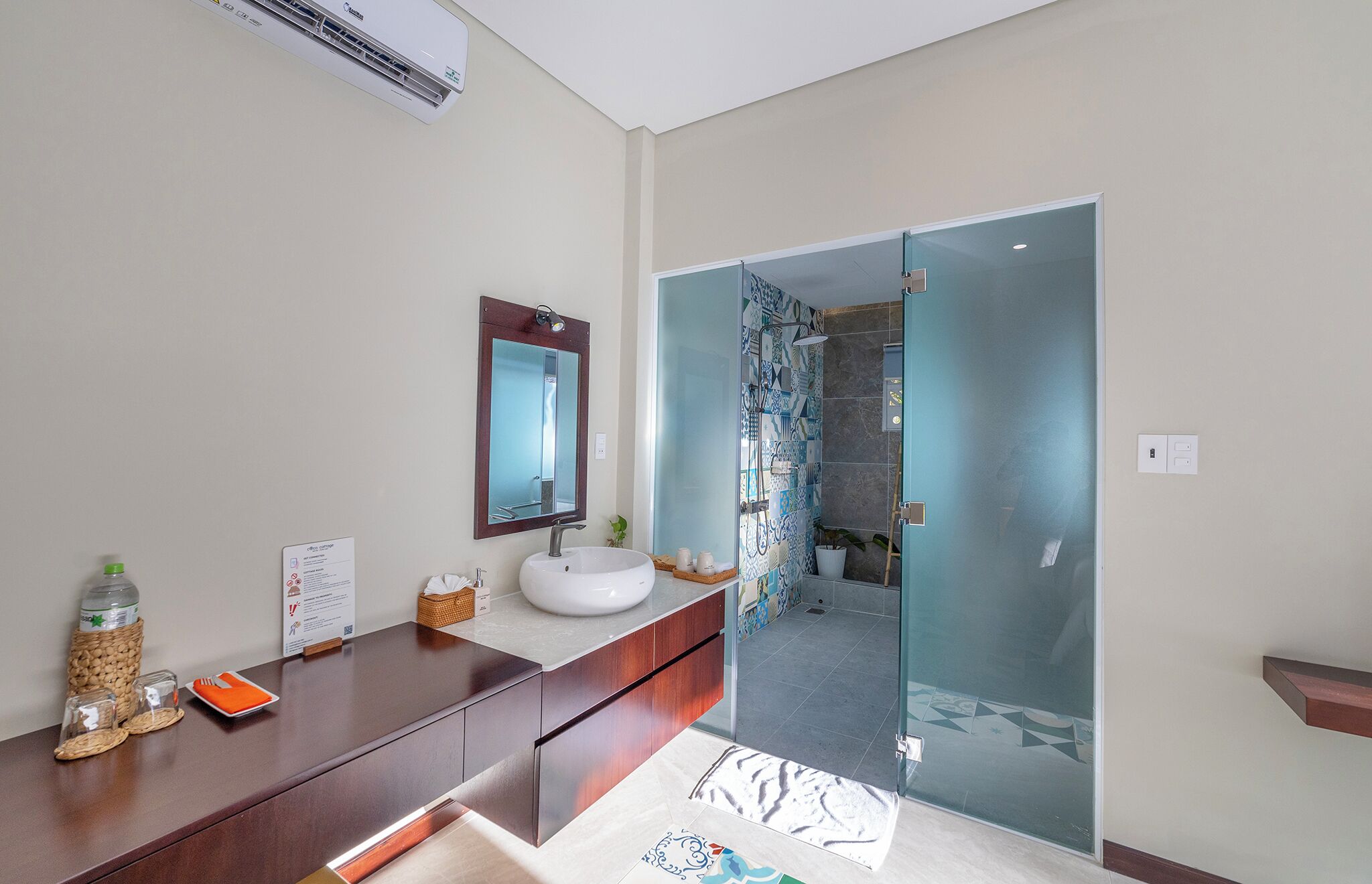 A modern bathroom with a wooden vanity, a white sink, a mirror, and a glass shower enclosure.