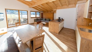 A spacious kitchen with wooden cabinets and a large island, a dining area with a wooden table and chairs, and large windows offering a view of the outdoors. - High-quality apartment with ski storage (Kleinarl)