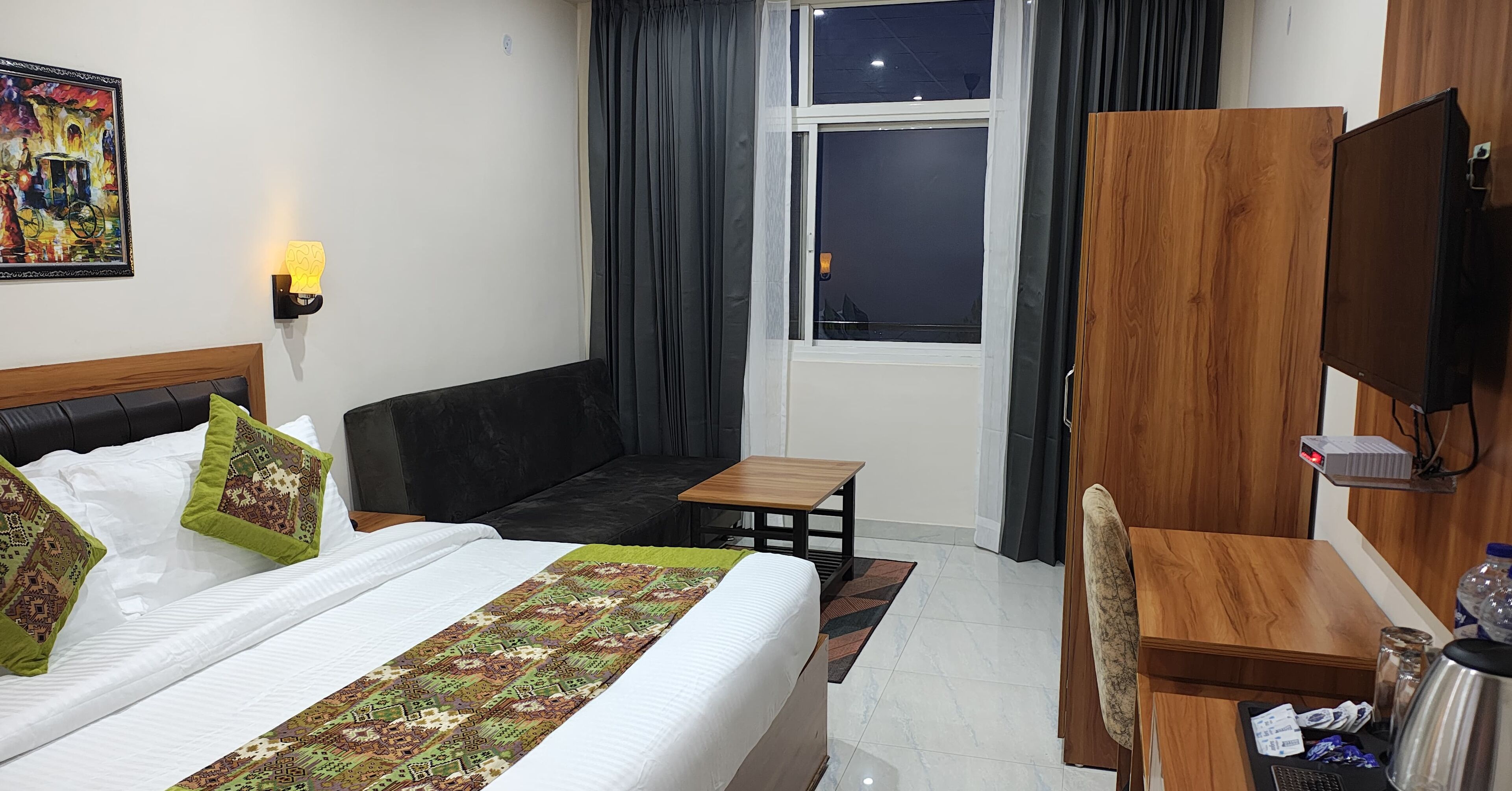 A hotel room with a bed, a sofa, a desk, a chair, a TV, and a window with curtains.