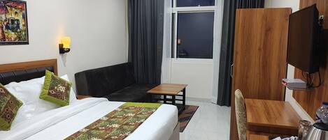 A hotel room with a bed, a sofa, a desk, a chair, a TV, and a window with curtains.