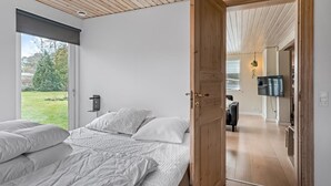 A bedroom with a large bed, a wooden door leading to an adjacent room, and a view of a garden through a window. - "Janna" - 200m from the sea by Interhome (Vordingborg)