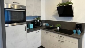 A modern kitchen with a built-in oven, microwave, and sink. There are cabinets, a countertop, and a hanging plant.