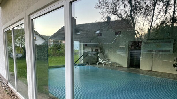 A swimming pool with a glass enclosure, a chair, and a ladder.