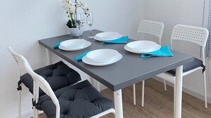 A dining table with white chairs, a vase with white flowers, and a framed quote on the wall.