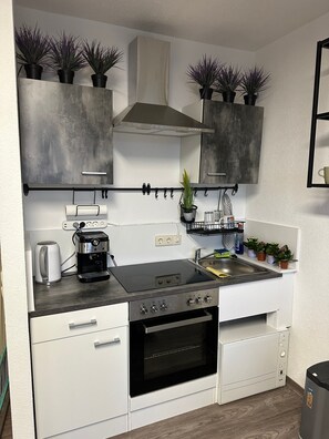 A compact kitchen with a built-in stove, oven, and coffee maker, featuring white cabinetry and potted plants.