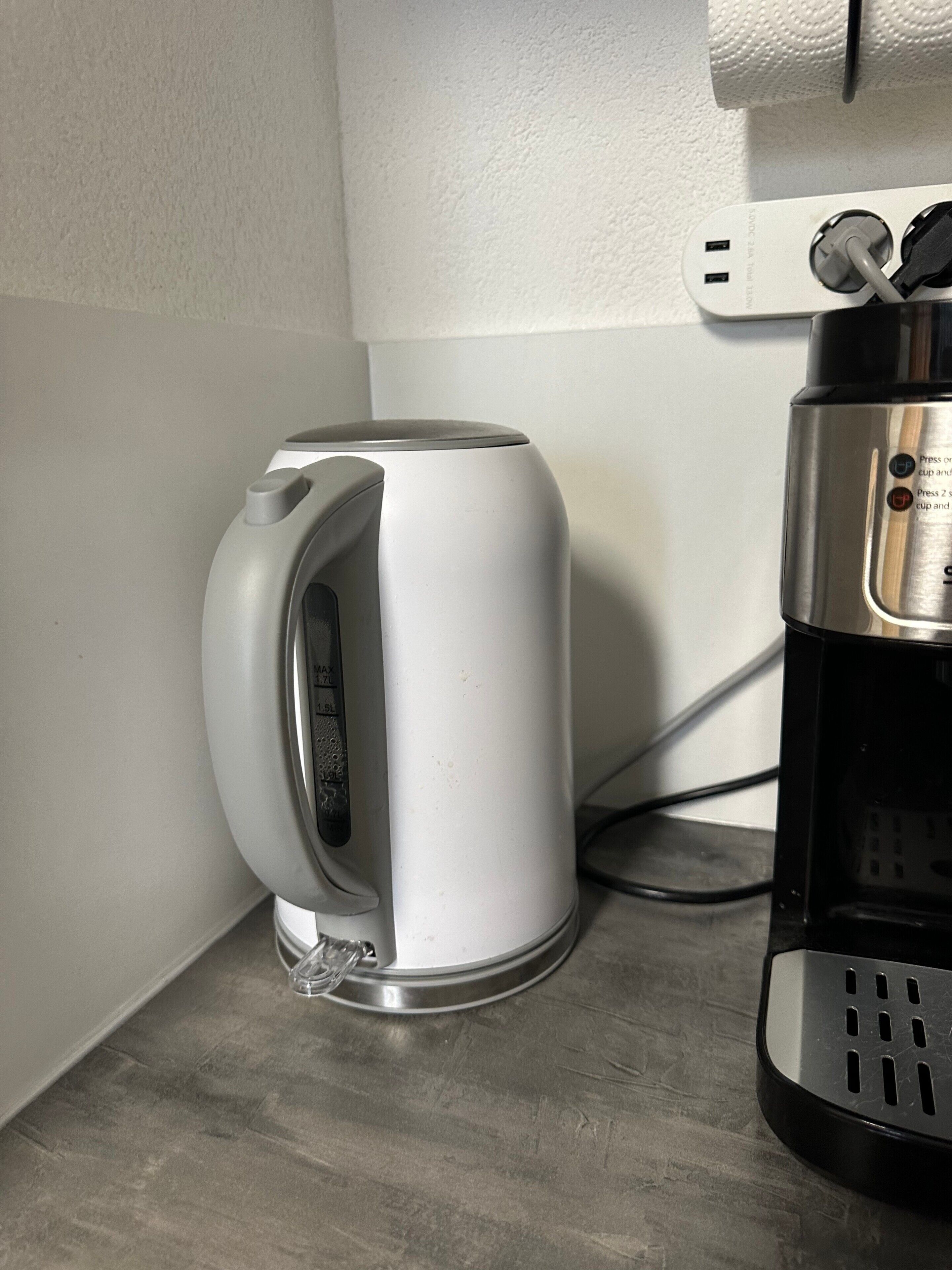 A white electric kettle and a black coffee maker on a countertop.