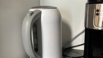 A white electric kettle and a black coffee maker on a countertop.