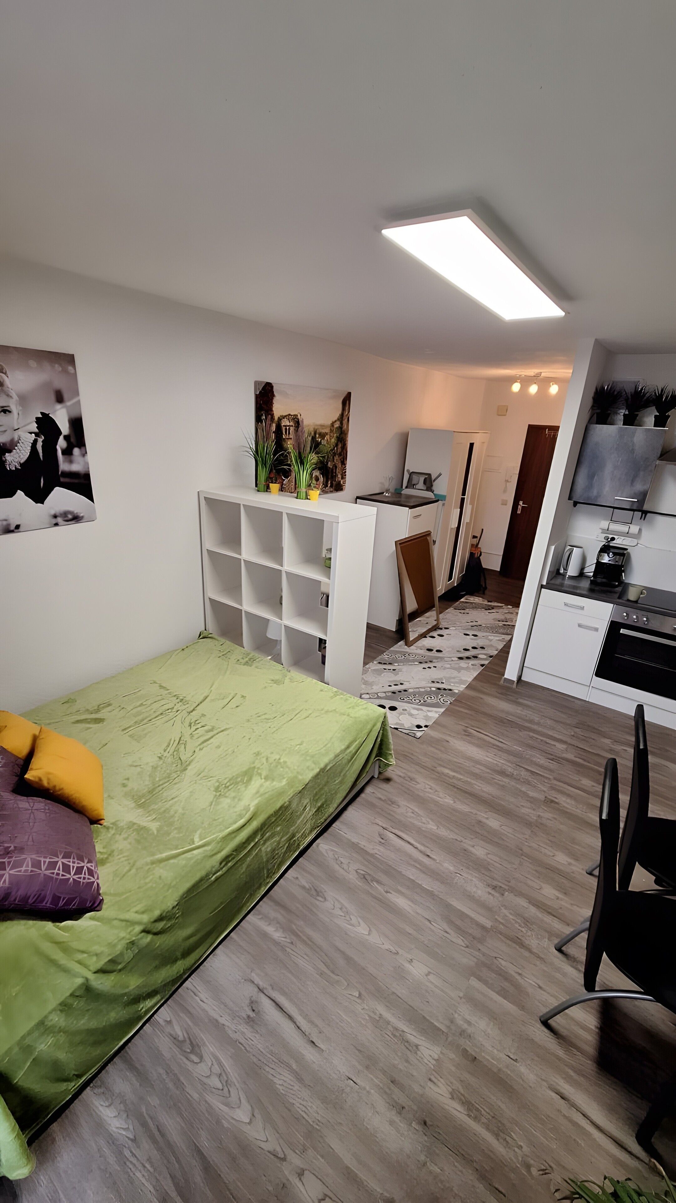 A bedroom with a bed, a desk, a chair, a kitchenette, and a bathroom.