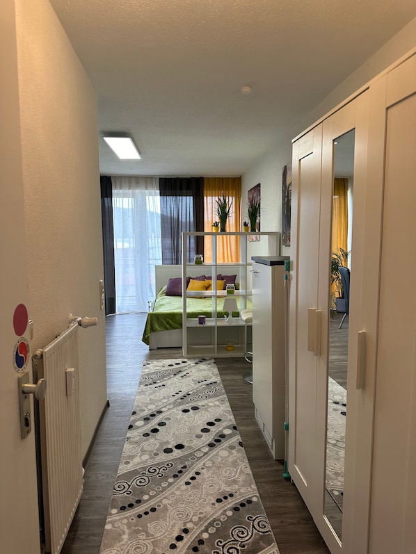 A narrow hallway leading to a bedroom with a bed, a radiator, and a patterned rug.