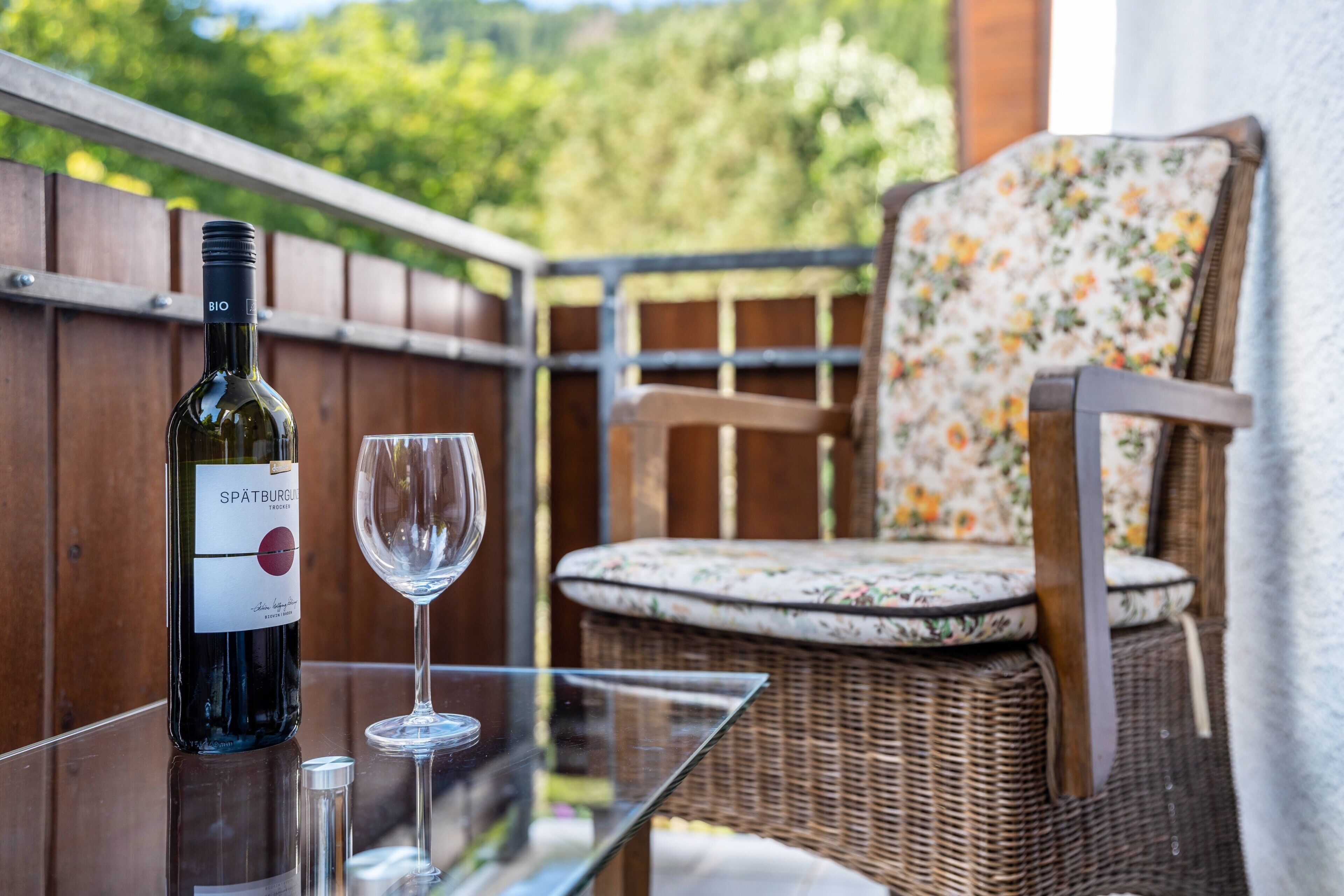 A bottle of Spätburgunder wine, a glass, and a wicker chair on an outdoor table.