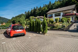 Ein rotes Auto steht auf einer gepflasterten Auffahrt vor einem Haus mit Balkon und Blumenkästen.