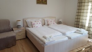 Ein Doppelbett mit floralen Kissen, ein Nachttisch mit Lampe, ein Sessel und ein Bild an der Wand.