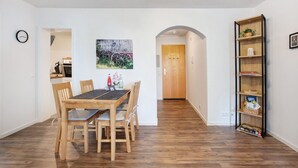 Uma área de jantar com mesa e cadeiras de madeira, um relógio na parede, um quadro e uma estante de livros.