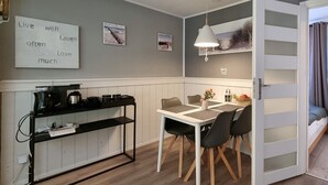 Cocina compacta con comedor, estación de café y vista de la habitación contigua a través de una puerta entreabierta.
