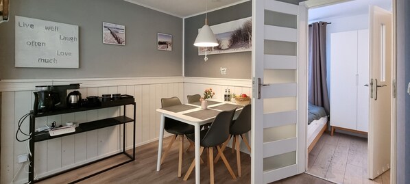 A compact kitchen with a dining area, a coffee station, and a view of the adjacent room through a partially open door.