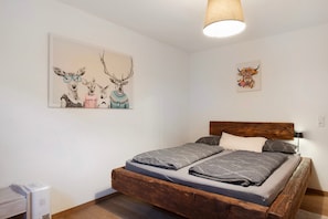 Un dormitorio con una cama de madera, una pared blanca y dos obras de arte en la pared.