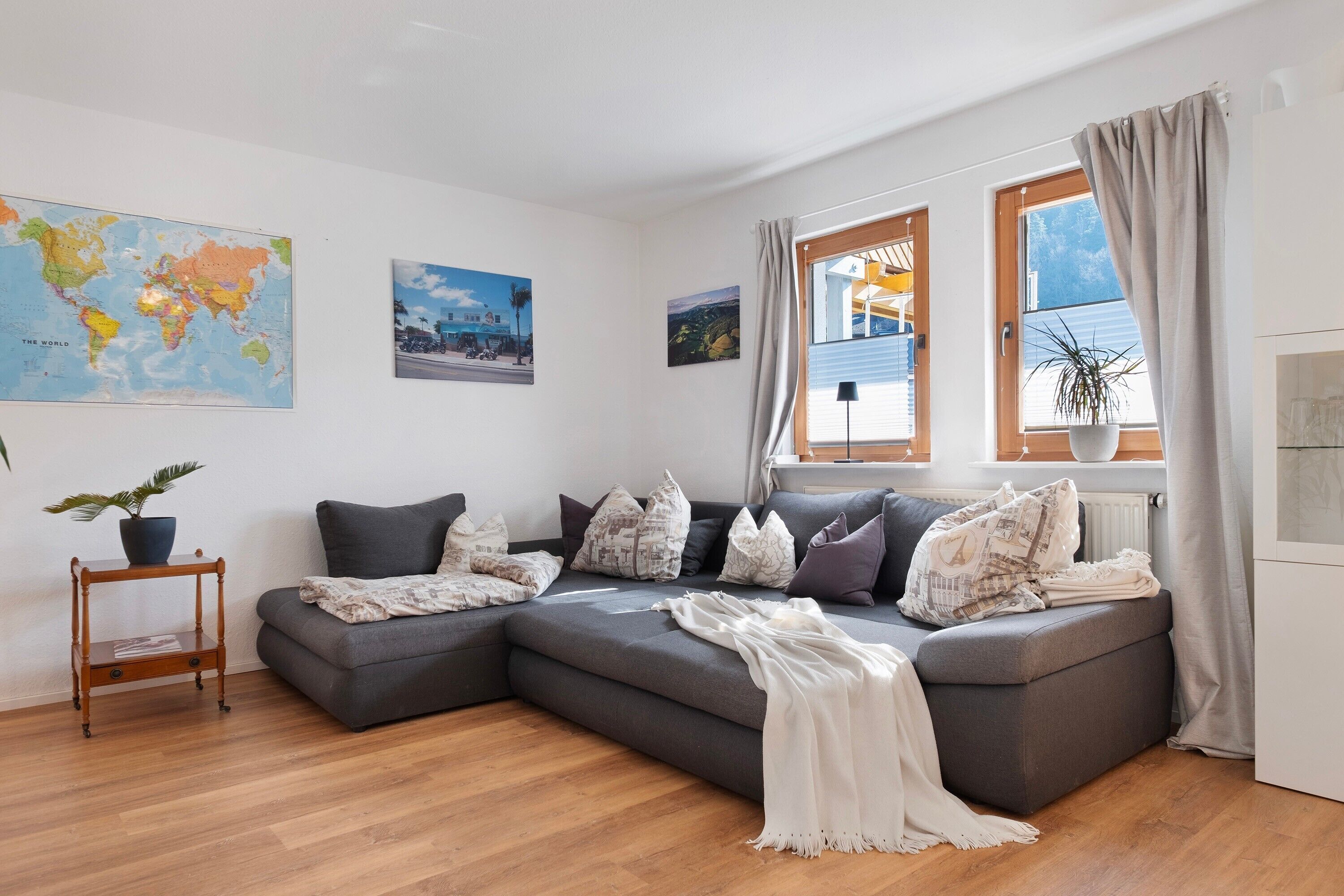 Ein modernes Wohnzimmer mit einem Ecksofa, einer Weltkarte und einem Fenster mit Vorhängen.