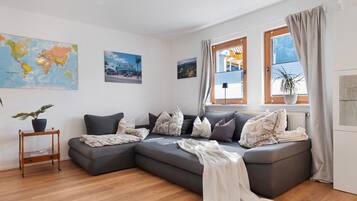 Ein modernes Wohnzimmer mit einem Ecksofa, einer Weltkarte und einem Fenster mit Vorhängen.
