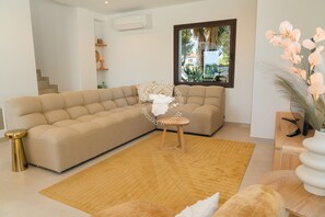 A modern living room with a beige sectional sofa, a small wooden stool, and a wooden floor rug. - CostaBlancaDreams - Casa Fuente Salvaje in Moraira (Moraira)