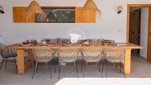 Un comedor con una mesa de madera dispuesta para seis personas, rodeado de sillas tejidas, con dos lámparas colgantes arriba.