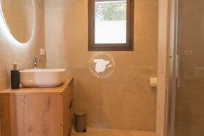 Une salle de bain avec un meuble-lavabo en bois, un lavabo blanc, un miroir, une fenêtre et un espace douche.