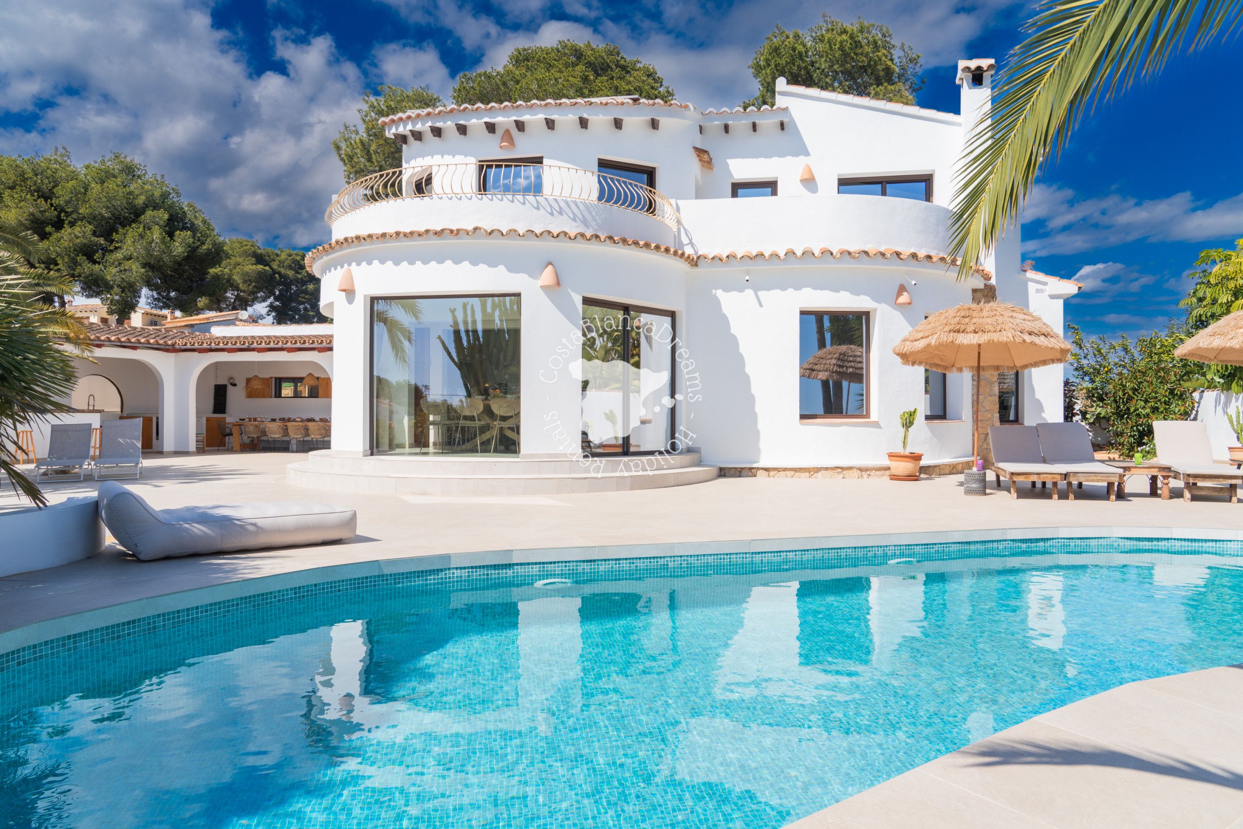 A modern villa with a swimming pool, large windows, and outdoor seating.