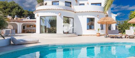 A modern villa with a swimming pool, large windows, and outdoor seating.