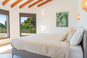 Une chambre avec un grand lit, une vue sur la verdure par la fenêtre et un tableau accroché au mur.