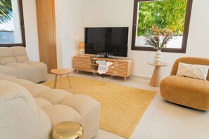 A modern living room with a flat-screen TV on a wooden console, beige sofas, a small round table, and a potted plant. - CostaBlancaDreams - Casa Fuente Salvaje in Moraira (Moraira)