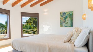 Un dormitorio con una cama grande, vistas a la vegetación por una ventana y un cuadro en la pared.