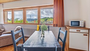 A room with a wooden ceiling, a dining table with chairs, a small kitchen area with a microwave, and a view of a landscape through large windows. - Haus Kehrwieder Studio with Panoramic Views, Hochschwarzwald Card, Wi-Fi, Parking (Todtnau)