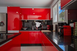 A modern kitchen with red cabinetry, a black and white tiled floor, and a stainless steel refrigerator.