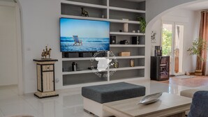 Moderni olohuone, jossa on litteänäyttöinen televisio, puinen kaappi ja harmaa penkki.