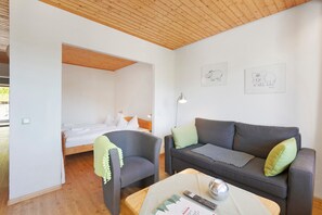 A room with a bed, a grey sofa, a chair, a lamp, and two wall art pieces.
