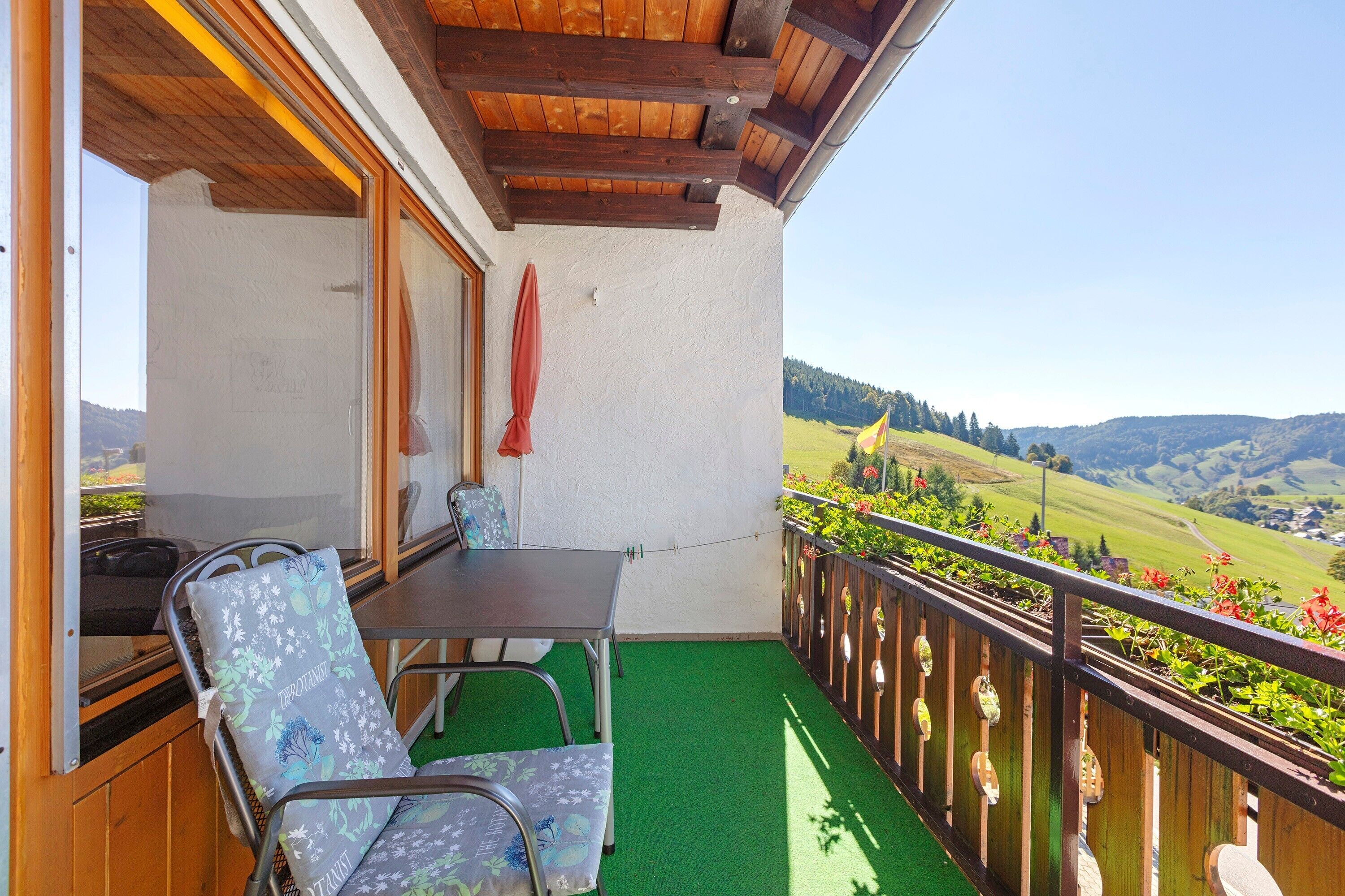 Ein Balkon mit Tisch und Stühlen, einer Holzbalkendecke und Blick auf eine grüne Landschaft.