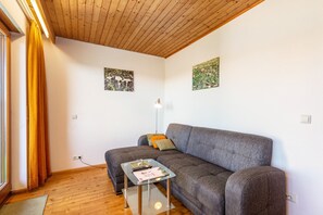 Un salon avec un canapé gris, une table basse en verre et deux tableaux encadrés accrochés au mur.