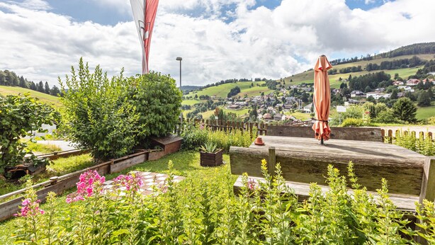 A garden with a wooden deck, a flag, and a view of a town in the background. - Haus Kehrwieder Apartment 3: Balcony, Mountain View, Hochschwarzwald Card, Wi-Fi, Parking (Todtnau)