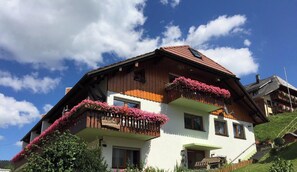 A two-story chalet with wooden balconies adorned with flowers, a sloped roof, and a clear sky.