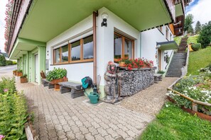Un bâtiment à l’extérieur verdoyant, avec un escalier en bois et un jardin agrémenté de plantes et de fleurs en pot.