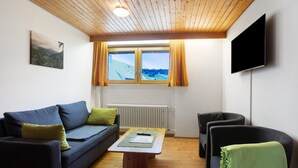 Una sala de estar con sofá, sillones, una mesa de centro, televisión y una ventana con cortinas.