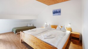 Un dormitorio con techo de madera, una cama con ropa de cama blanca, un sofá verde y una mesita de noche pequeña.