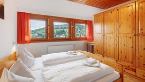 Een slaapkamer met twee bedden, een houten garderobe en uitzicht op een groen landschap.