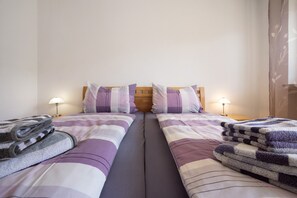 Cama doble con cabecera de madera, dos mesitas de noche con lámparas y una toalla doblada a cada lado.