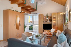A living room with a sofa, armchairs, a coffee table, a TV, wooden cabinets, and a balcony with glass doors. - Apartment '45qm' with Balcony, Wi-Fi and Air Conditioning (Sasbach am Kaiserstuhl)