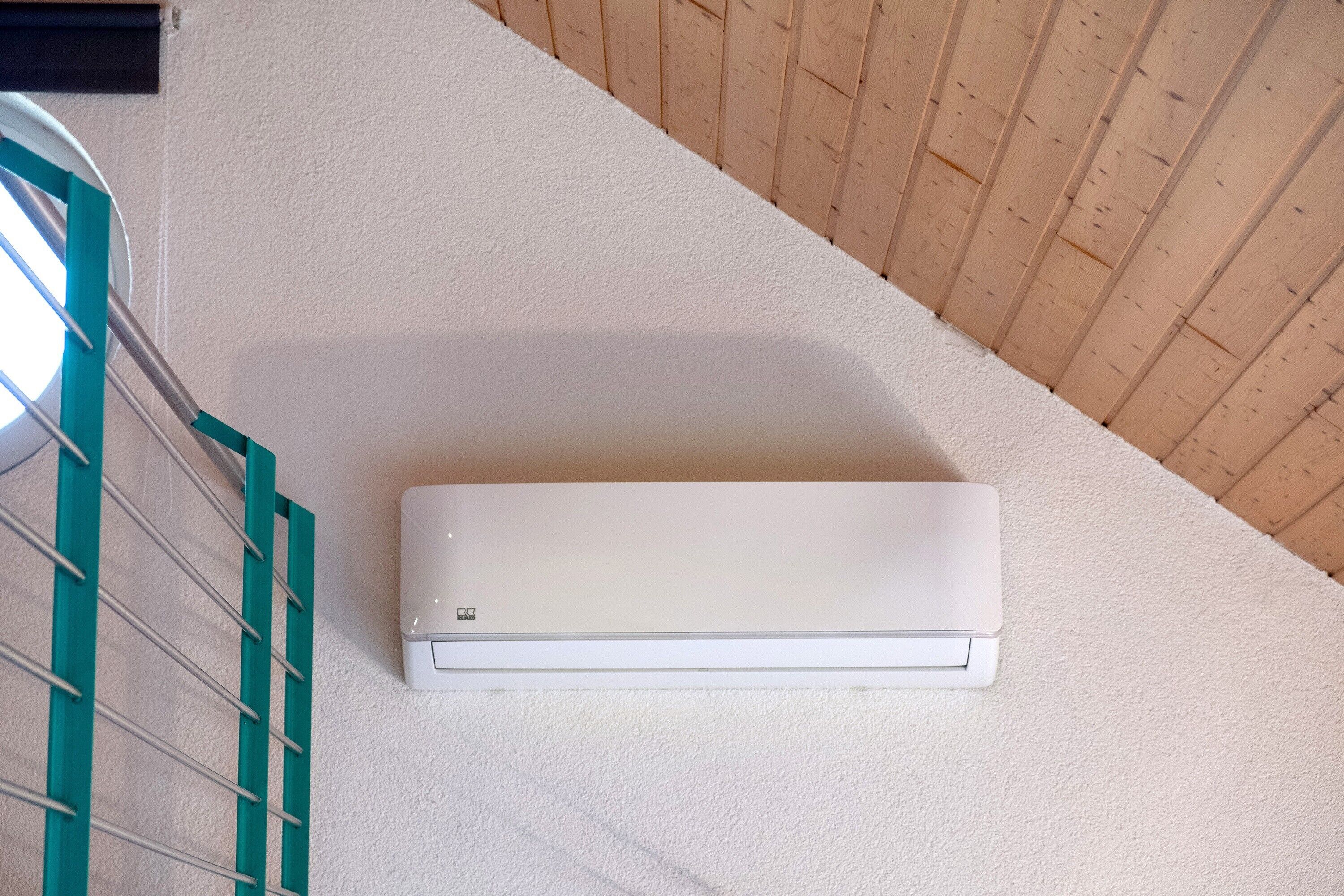 Een witte airconditioningunit bevestigd aan een structuurwand met een houten plafond.
