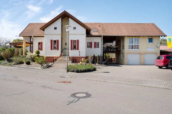 A two-story building with a red-tiled roof, a garage, and a sign indicating a business. - Apartment '45qm' with Balcony, Wi-Fi and Air Conditioning (Sasbach am Kaiserstuhl)
