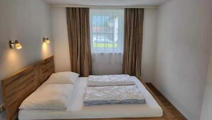 A neatly made bed with a wooden headboard, two bedside lamps, and a window with curtains. - Holiday Home in Holzgau near Snowworld Ski Area (Holzgau)